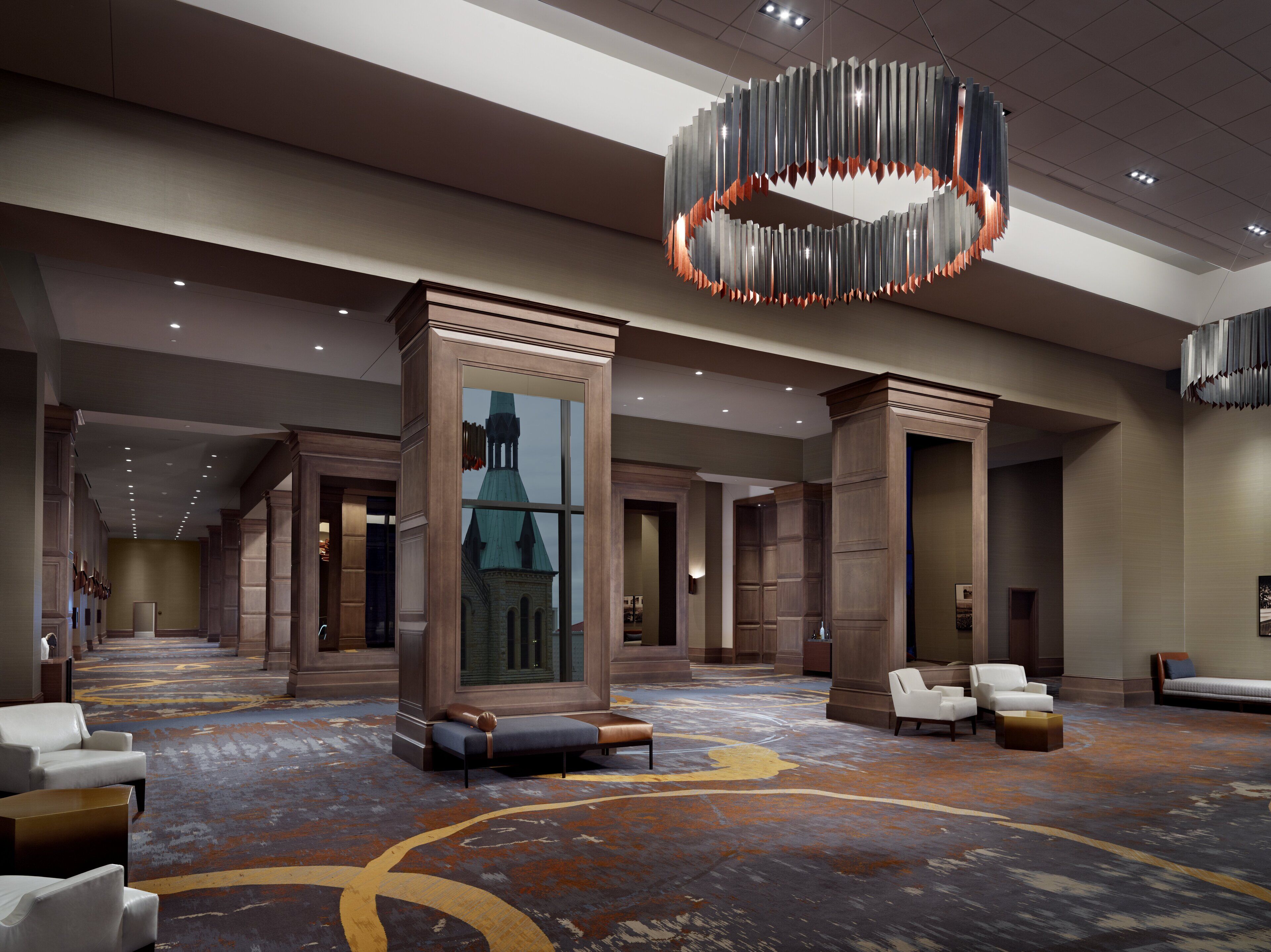 A spacious lobby with a large chandelier, seating areas, and a view of a building through a glass wall.