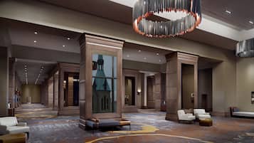 A spacious lobby with a large chandelier, seating areas, and a view of a building through a glass wall.