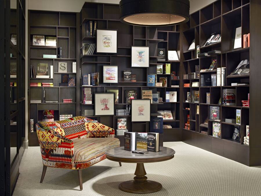 A library with bookshelves, a patterned armchair, and a table with books.