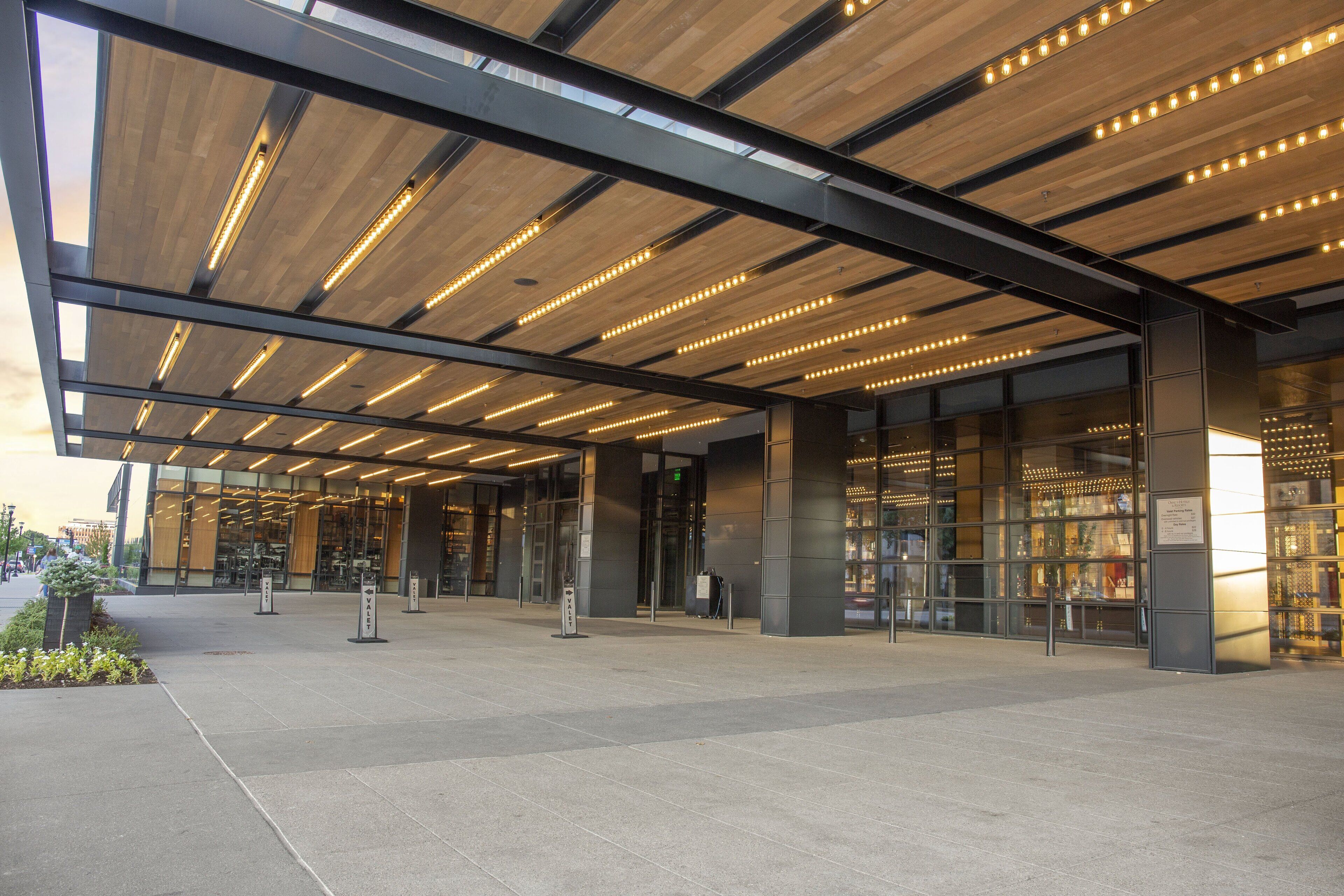 A modern building entrance with a covered walkway, glass doors, and a well-lit interior.