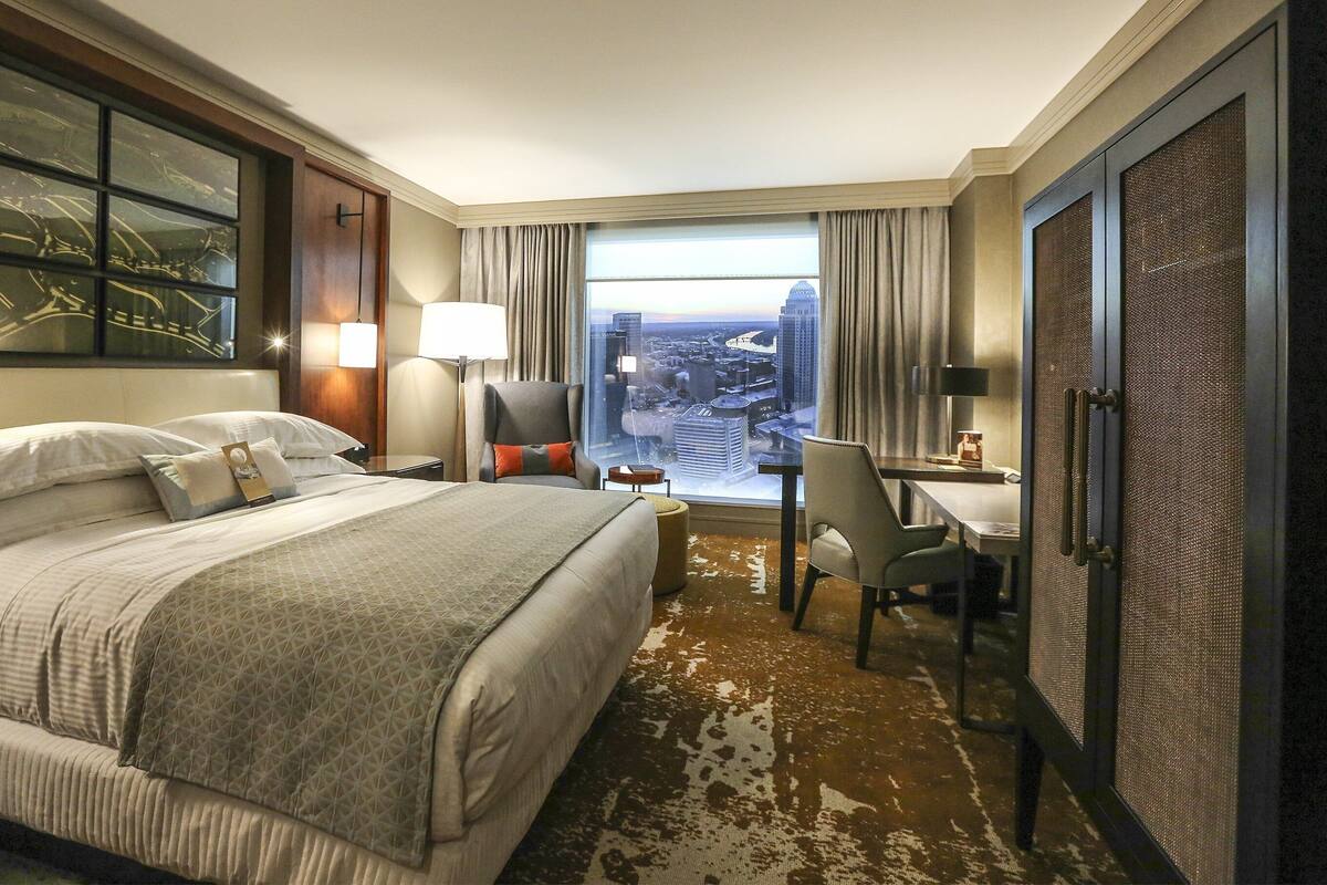 A hotel room with a large bed, a desk, and a view of the cityscape through the window.