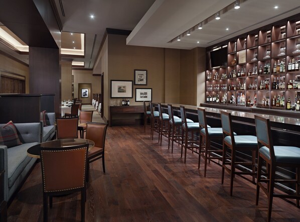 Un área de bar con suelo de madera, taburetes y una pared llena de botellas de licor.