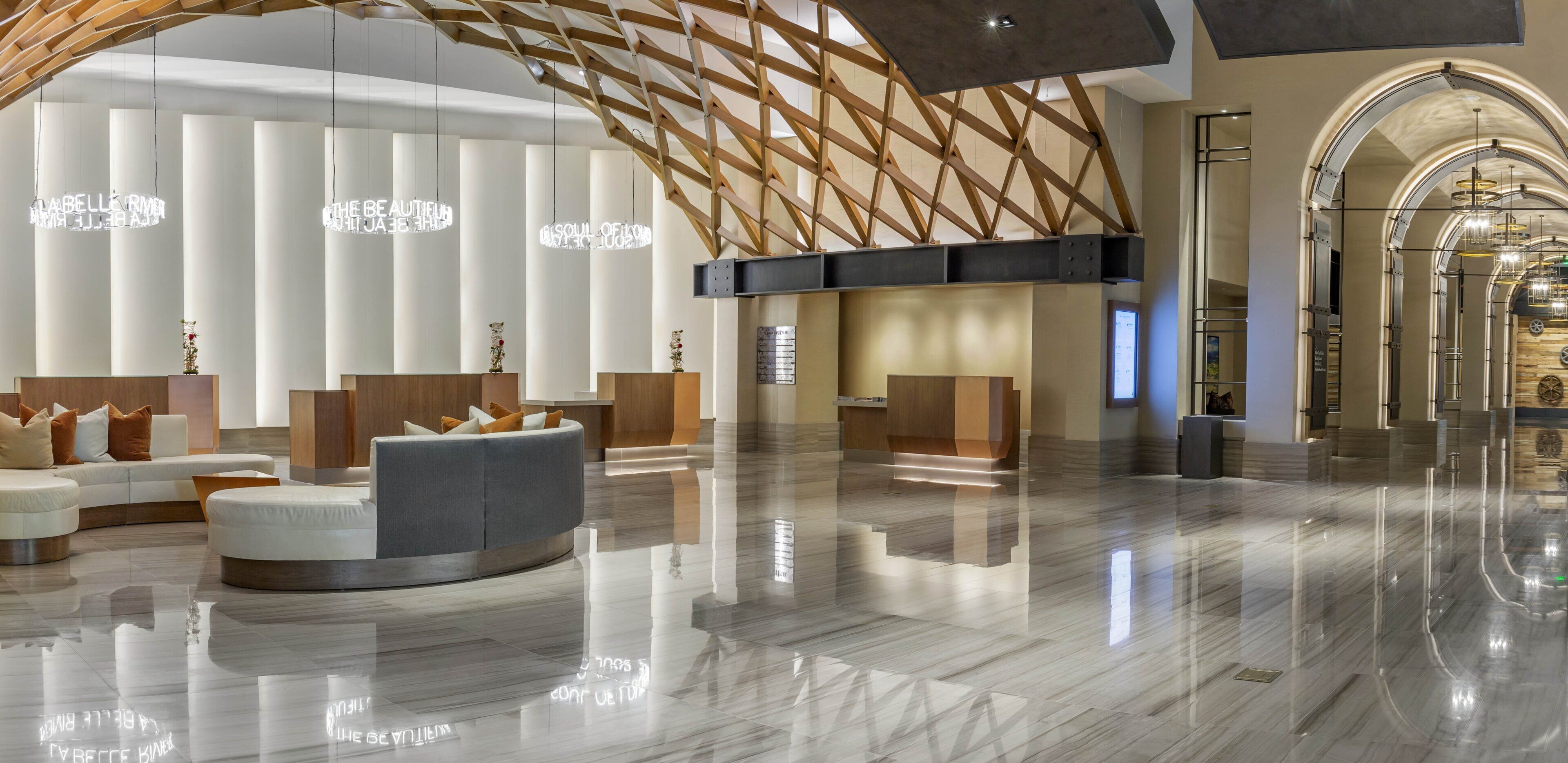 A modern lobby with a curved seating area, a wooden ceiling structure, and a polished marble floor.
