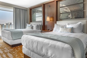 Habitación de hotel con dos camas, un ventanal grande con vista a la ciudad y una puerta de madera.