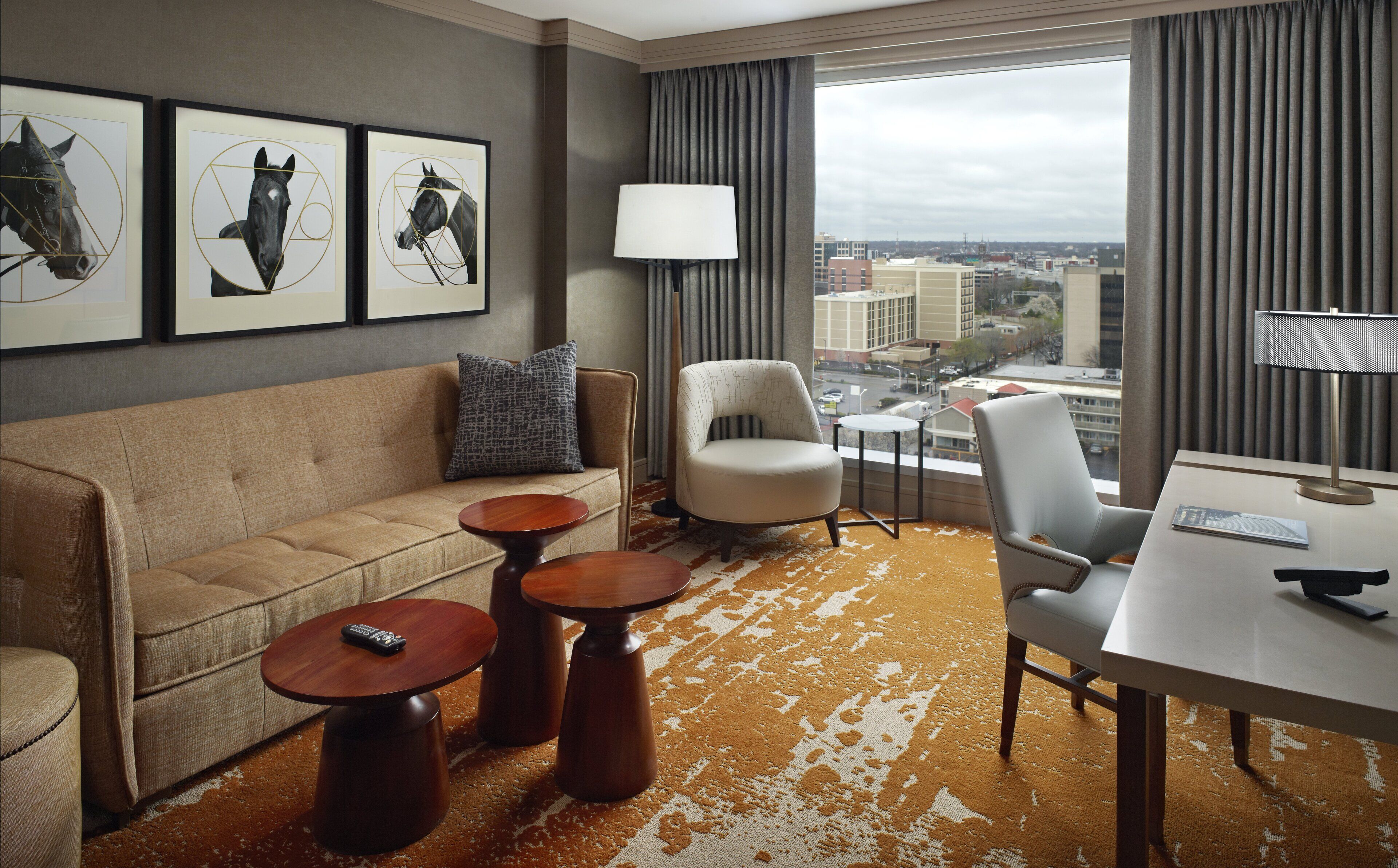 Quarto de hotel moderno com sofá, poltronas, mesa de jantar, abajur e obras de arte na parede.