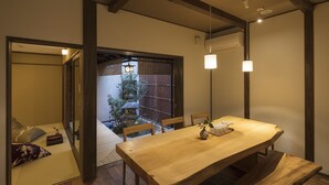 Ett traditionellt japanskt rum med tatamimattor på golvet, ett lågt träbord och en skjutdörr som leder ut till ett utomhusområde med utsikt över en trädgård och en traditionell port.