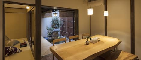 Una habitación tradicional japonesa con suelo de tatami, una mesa de madera baja y un puertas correderas que dan a un área exterior con vistas a un jardín y una puerta tradicional.