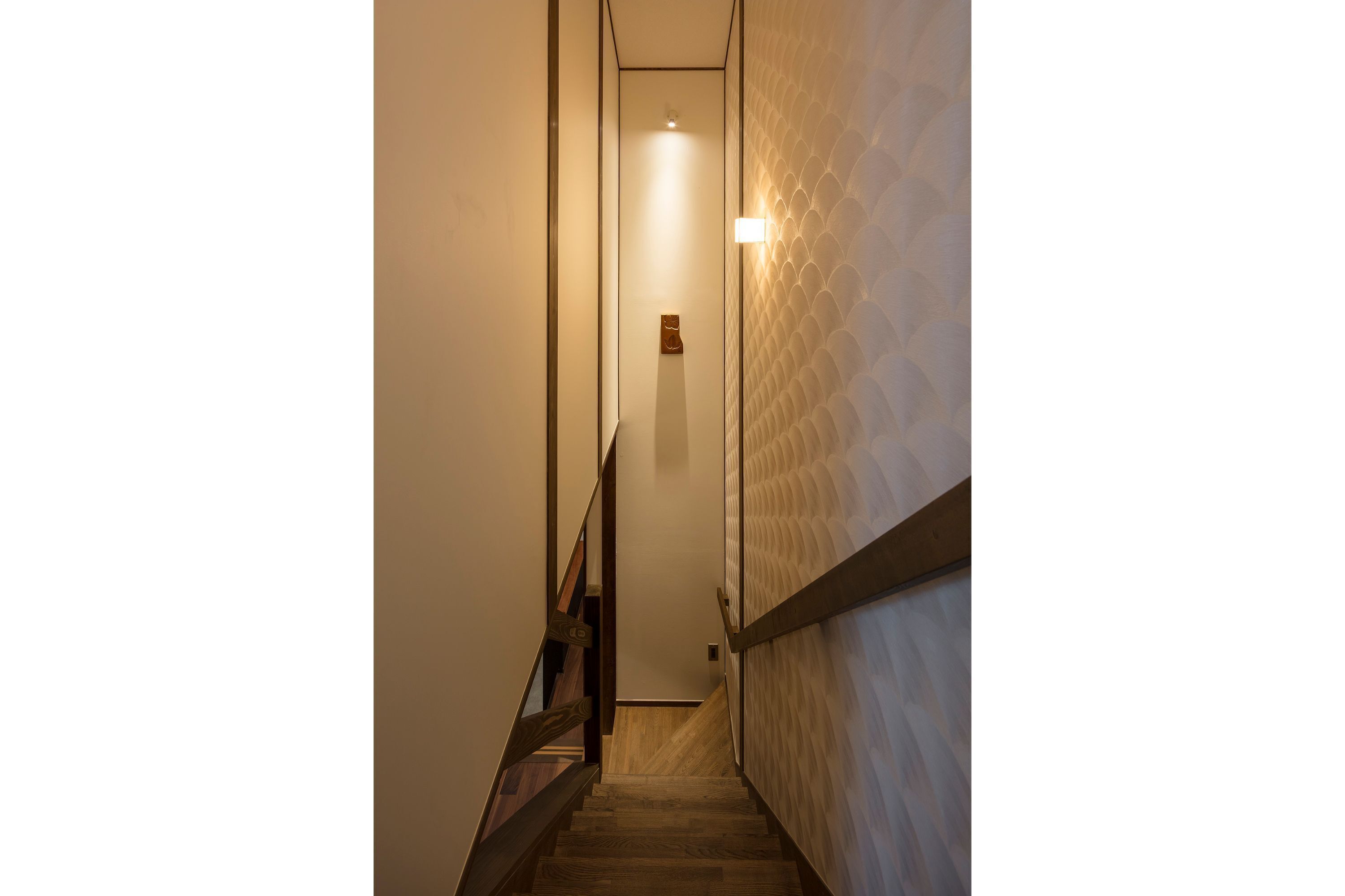 Un pasillo estrecho y bien iluminado con suelo de madera y una pared texturizada a la derecha.