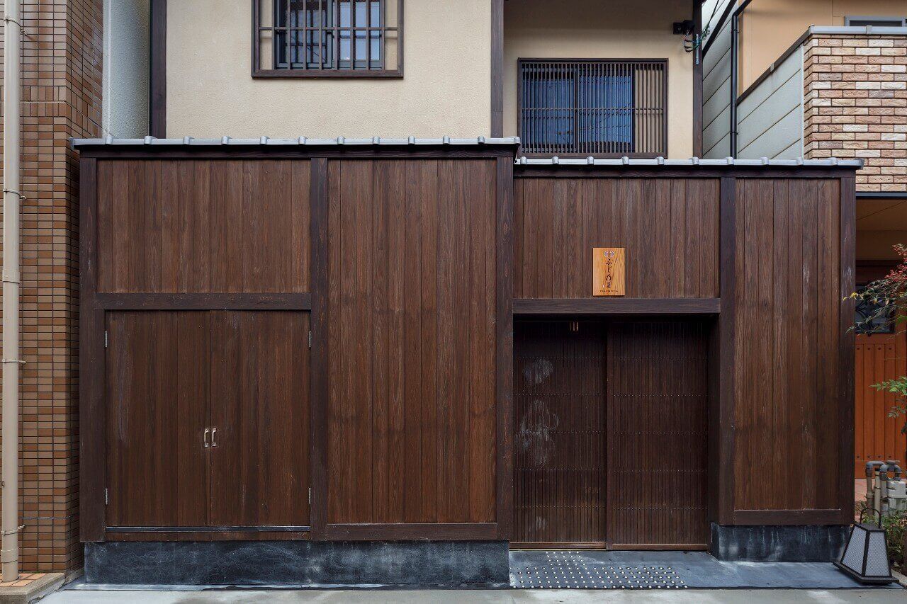 A wooden gate with a metal plaque, a tiled wall, and a window with bars.