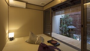 Ett traditionellt japanskt rum med tatamimattor på golvet, ett lågt bord med en lykta och en skjutdörr som leder ut till ett utomhusområde med ett trästaket och en stenlykta.