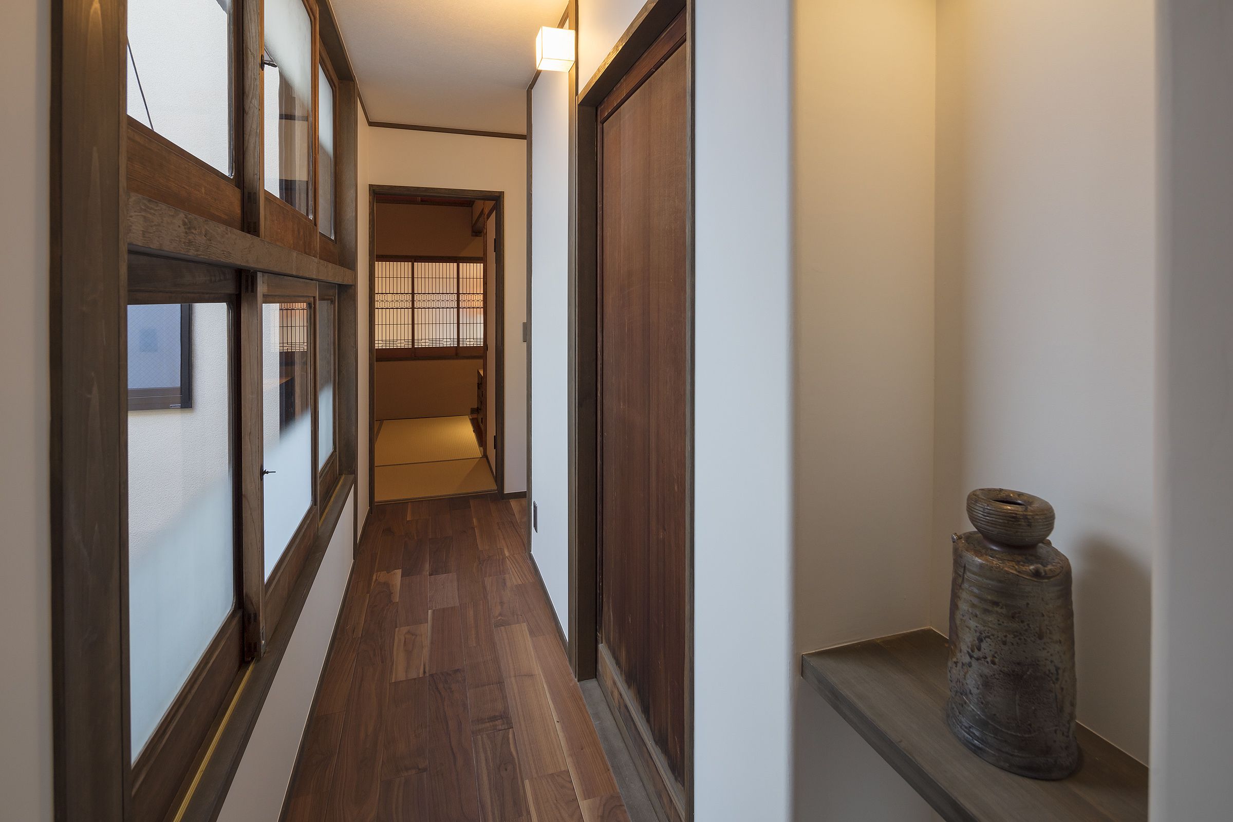 A narrow hallway with wooden flooring and a large wooden door on the right.