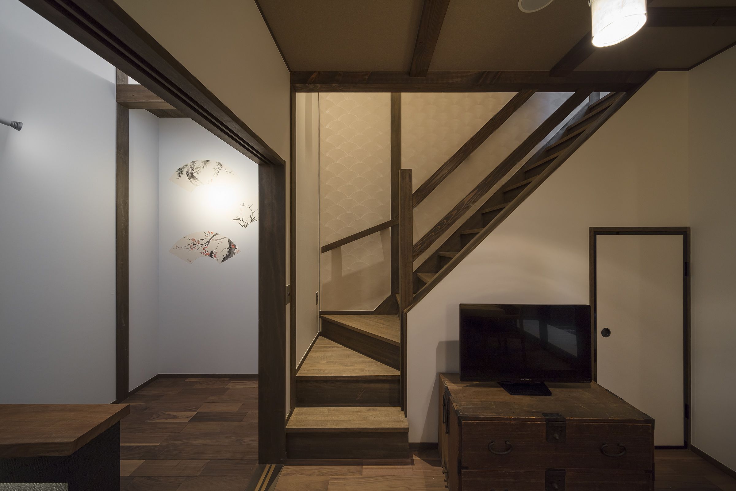 A staircase with wooden steps and a modern design, leading to a room with a television on a wooden cabinet.