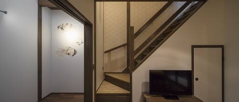 A staircase with wooden steps and a modern design, leading to a room with a television on a wooden cabinet.