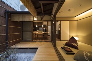 Una habitación tradicional japonesa con suelo de tatami, una mesa baja de madera y una puerta corrediza que da a una zona de cocina.