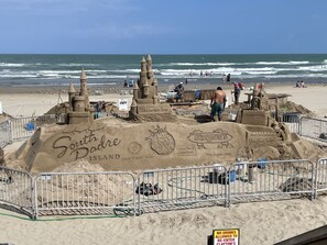 A sandcastle competition on a beach with various sand structures and a sign indicating no drinks allowed to re-enter Clayton's.