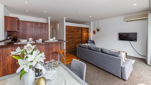 A modern kitchen with wooden cabinets, a dining area with a glass table, and a grey sofa in a living room. - Premium 1BR Apartment at Princes Wharf (Auckland)