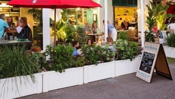 An outdoor café with tables and chairs, surrounded by greenery and covered by striped awnings. - Premium 1BR Apartment at Princes Wharf (Auckland)