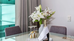 A glass table with a bottle of champagne, a vase of white lilies, and two champagne flutes on a tray. - Premium 1BR Apartment at Princes Wharf (Auckland)