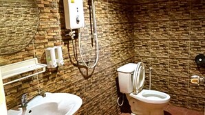 A bathroom with a stone wall, a sink, a toilet, and a shower. - View Garden Resort (Ko Phi Phi)