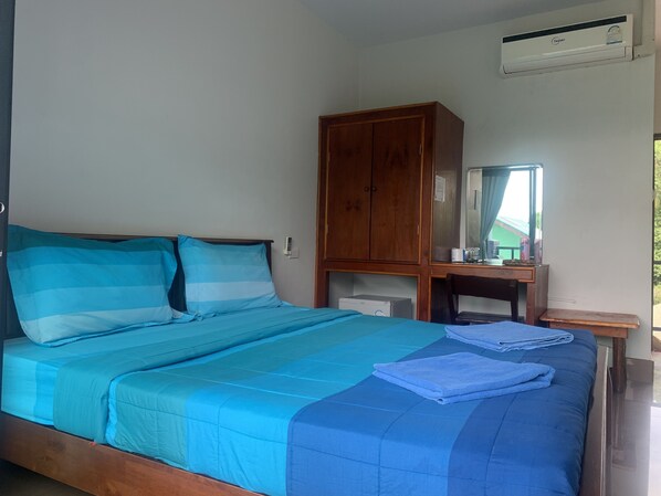 A bed with blue bedding, a wooden wardrobe, a desk with a mirror, and an air conditioning unit. - View Garden Resort (Ko Phi Phi)