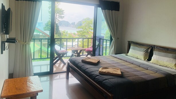 A bedroom with a bed, a small table, and a balcony with a view of a body of water and greenery. - View Garden Resort (Ko Phi Phi)