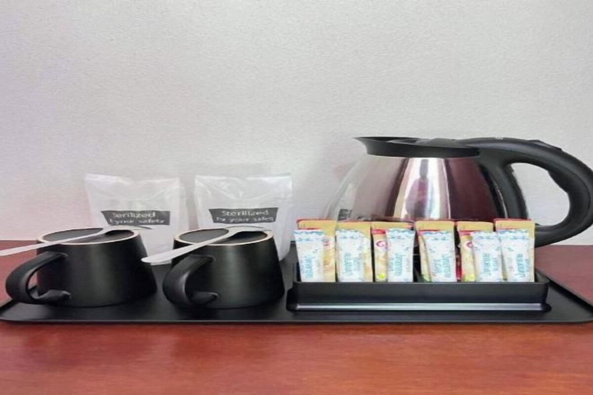 A coffee station with two black mugs, a coffee pot, and a tray of packaged coffee.