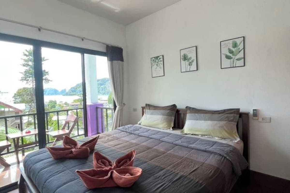 A bedroom with a large bed, a balcony with chairs, and framed botanical prints on the wall.