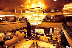 A spacious lobby with a central reception desk, seating areas, and a large chandelier.