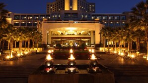 Entrada de hotel con un arco imponente, palmeras y una fuente con velas.