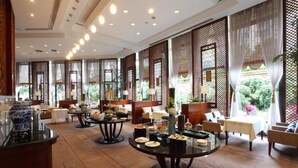 Un amplio vestíbulo de hotel con varias zonas de estar, que incluyen mesas redondas y sofás, y ventanas grandes con paneles decorativos.
