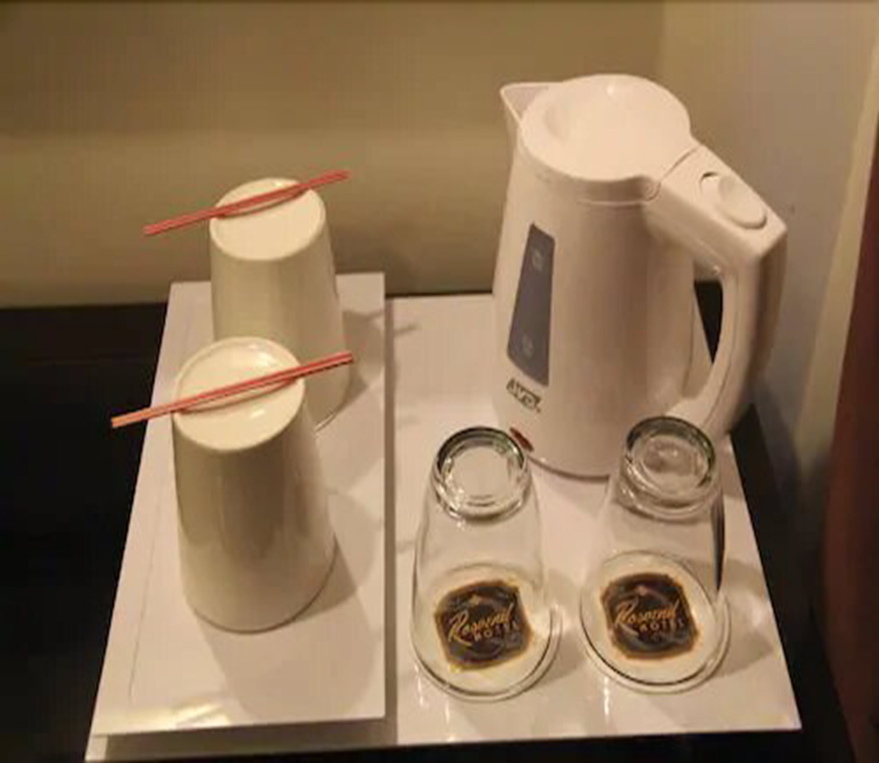 Un plateau avec un pichet blanc, deux tasses et deux petits verres à liqueur, ainsi qu’une étiquette indiquant le type de boisson.