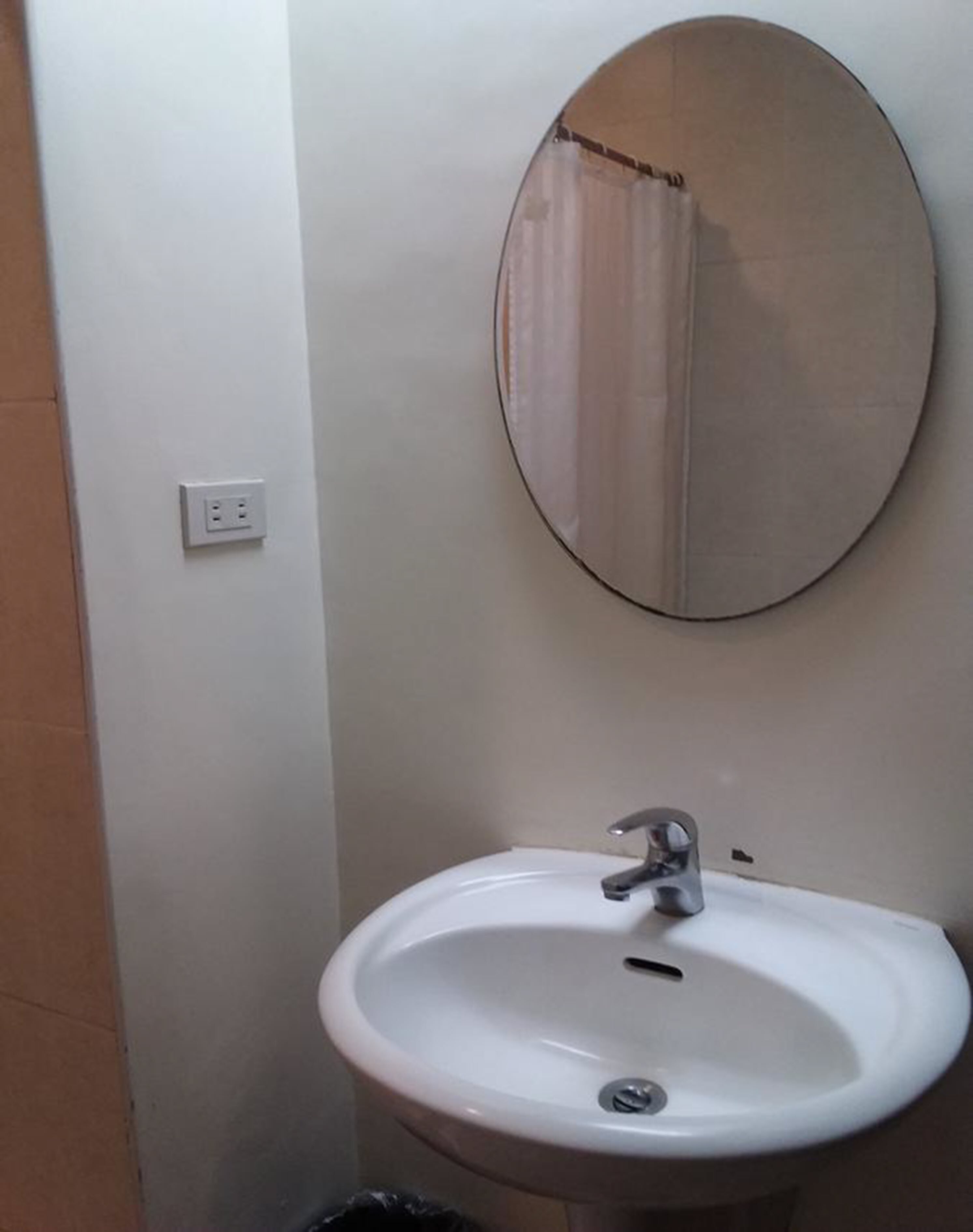 A bathroom with a white sink, a round mirror, and a light switch on the wall.