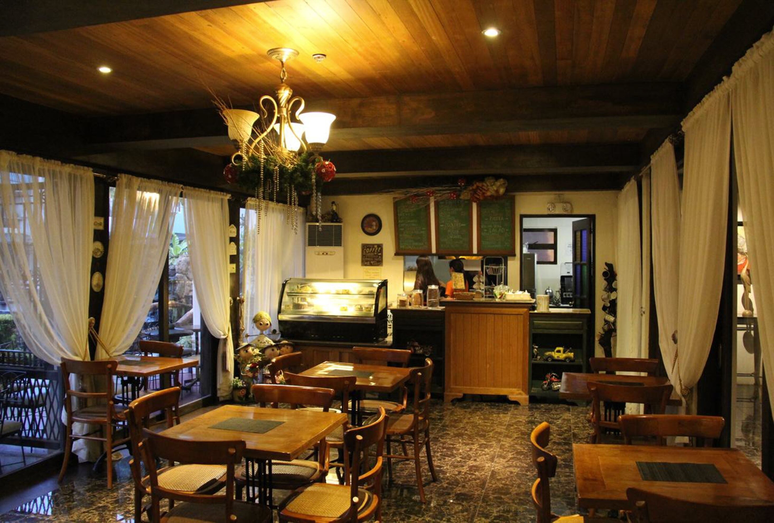 A restaurant with wooden tables and chairs, a bar area, and a kitchen visible in the background.