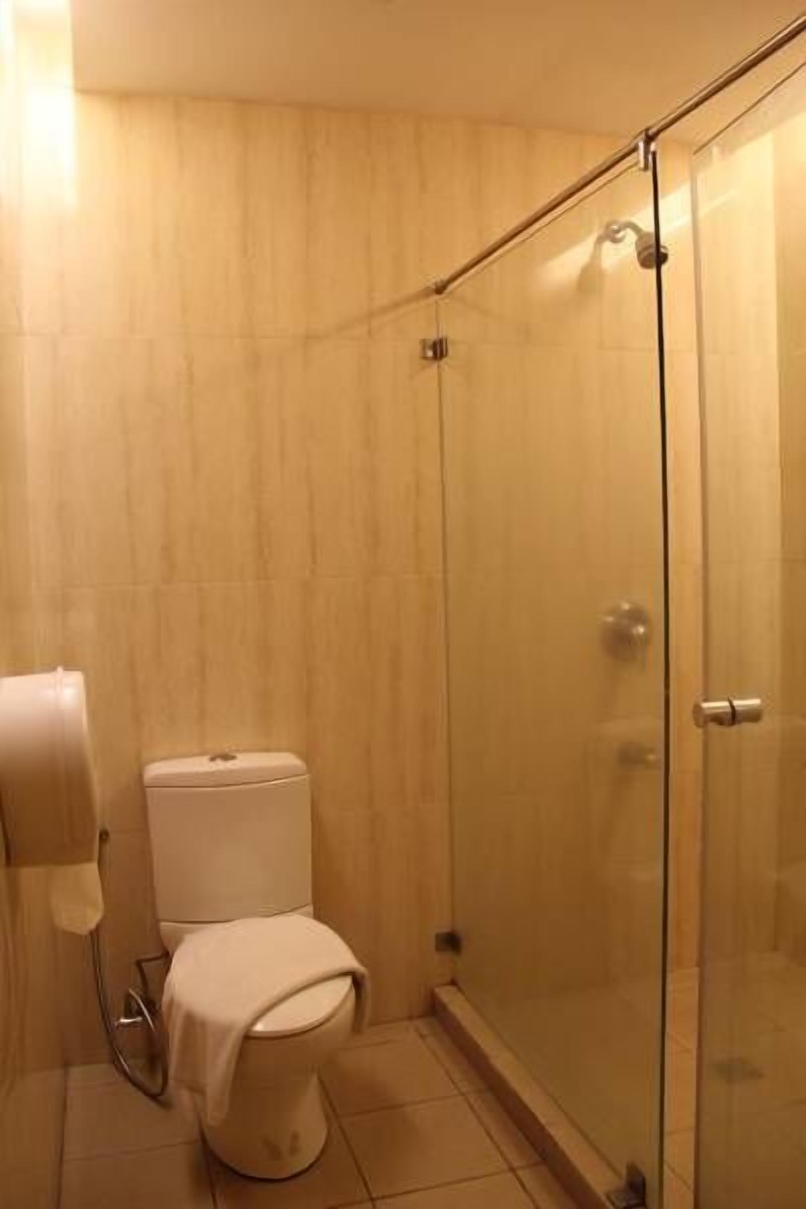 A bathroom with a toilet, a glass shower enclosure, and a towel dispenser.