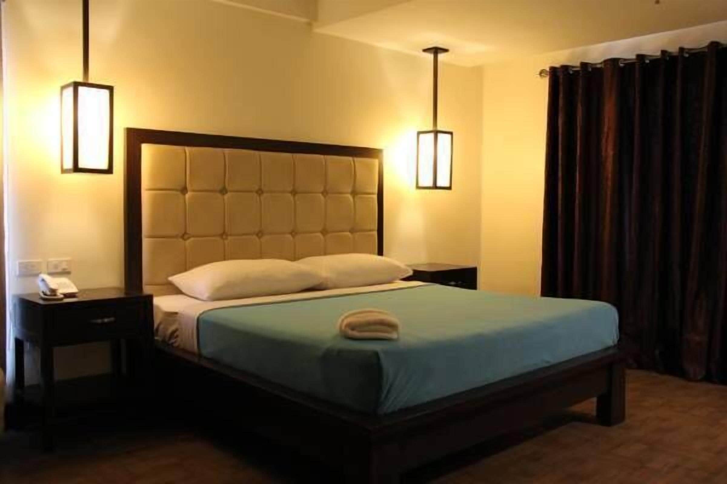 Une chambre d’hôtel avec un grand lit, deux tables de chevet, une petite table et une lampe fixée au mur.