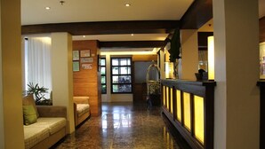 Een hotellobby met een marmeren vloer, een receptiebalie met een glazen scheiding en een bank met een kussen.