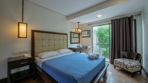 Een hotelkamer met een groot bed, nachtkastje met telefoon, een stoel en een balkon met gordijnen.