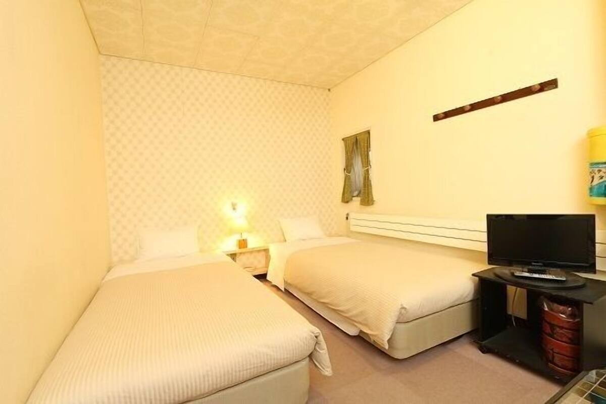 A hotel room with two beds, a television, and a nightstand.