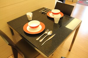 A dining table with a granite top, set with plates, cups, bowls, forks, knives, and spoons.