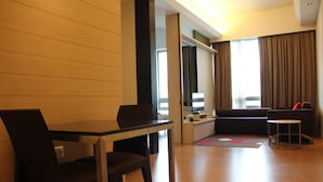 Une chambre d’hôtel moderne avec un plancher en bois, une table à manger avec des chaises, un canapé, une petite table d’appoint et une vue sur la ville grâce à de grandes fenêtres.