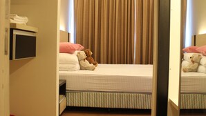 Une chambre d’hôtel avec un lit, un miroir, une télévision et une poubelle rouge.