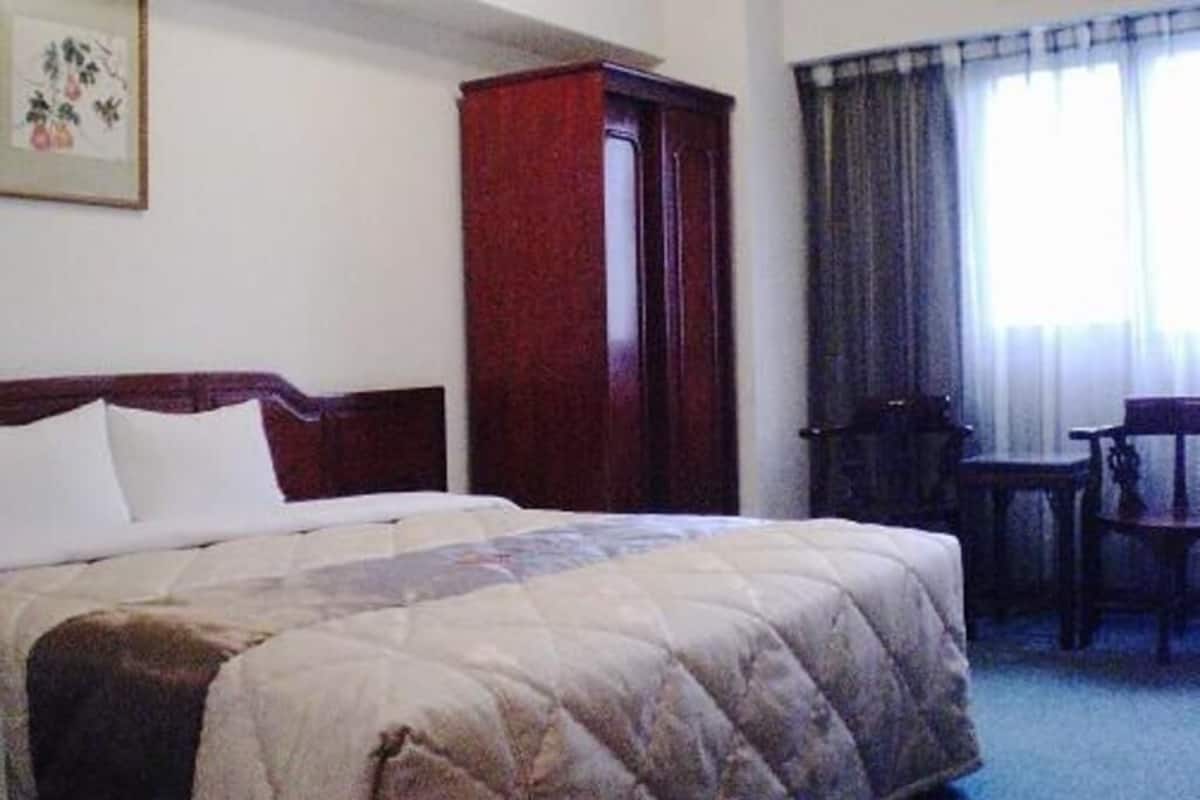 A hotel room with a bed, a wooden wardrobe, a desk, and a chair.