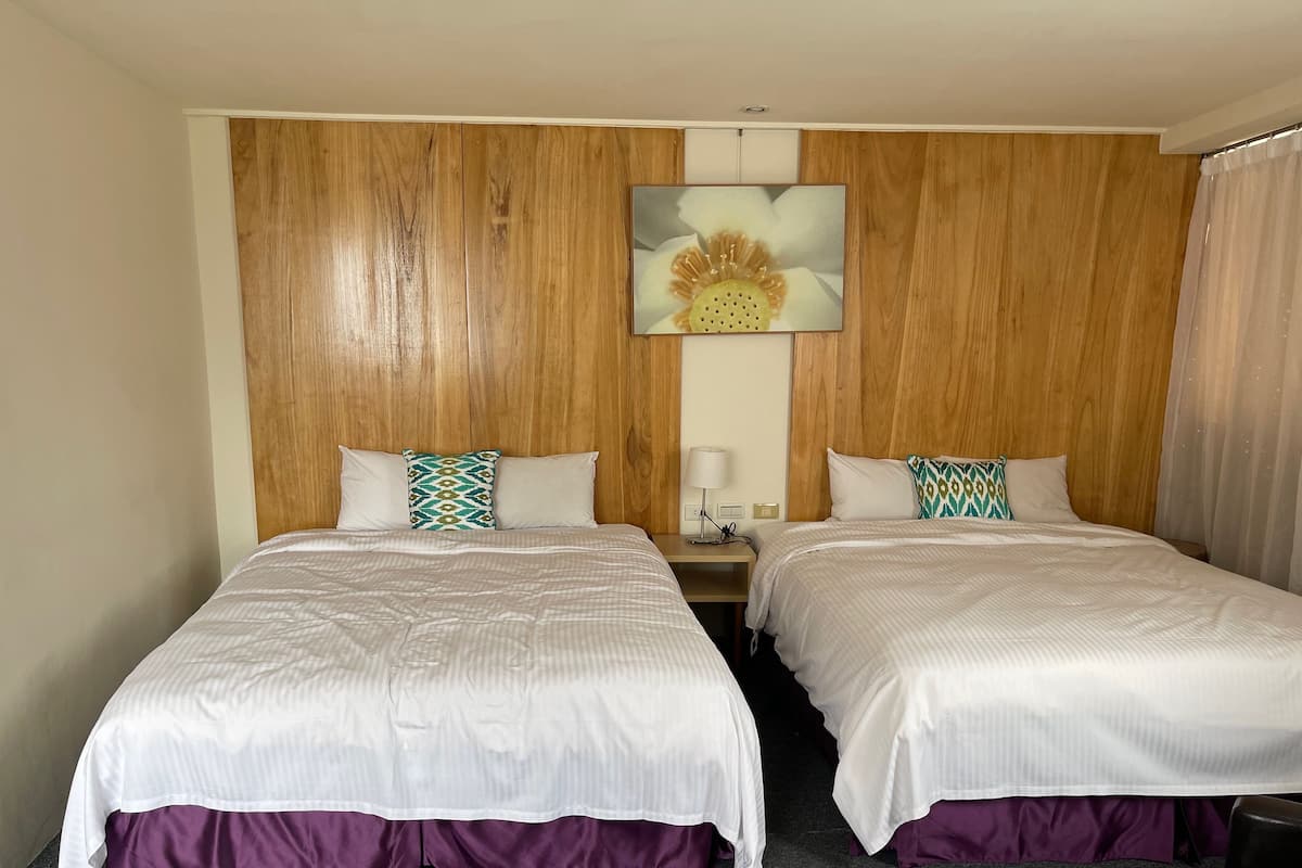 A hotel room with two beds, wooden paneling on the walls, a painting of a flower, and a nightstand with a lamp.