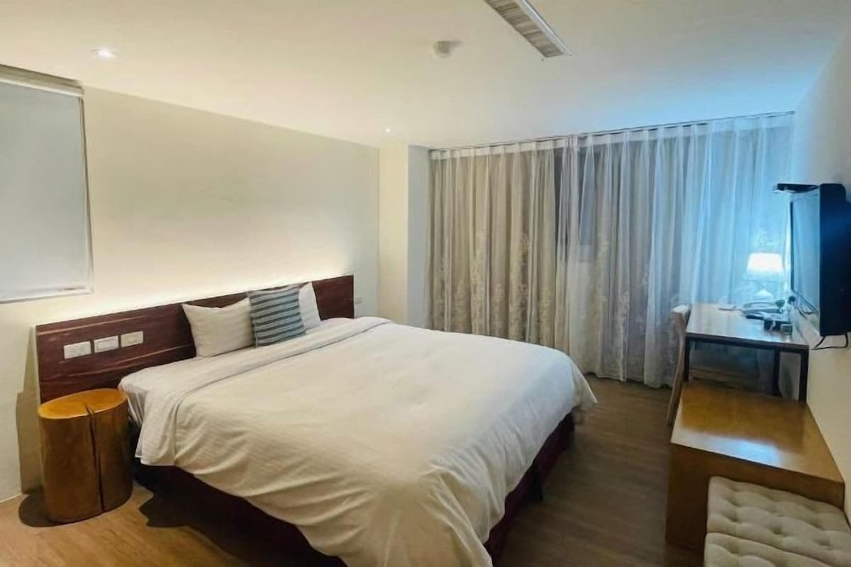 A hotel room with a large bed, a bedside table, a TV, and a window with curtains.