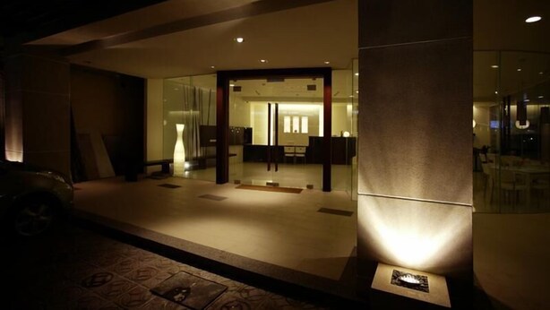 Entrada de hotel com porta de vidro, balcão de recepção e área de estar visível no interior.