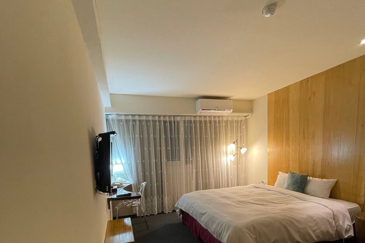 A hotel room with a bed, a desk, a chair, a TV, and a window with curtains.