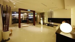 Um hall de hotel moderno, com balcão de recepção, entrada por porta de vidro e decoração minimalista.