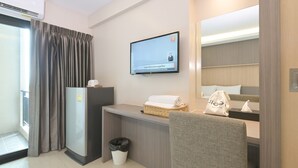 Une chambre d’hôtel moderne équipée d’un téléviseur à écran plat fixé au mur, d’un petit bureau avec un panier et une serviette, d’une chaise, d’une poubelle et d’un grand miroir.