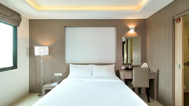 Une chambre d’hôtel avec un grand lit, une table de chevet, un bureau avec une chaise, un miroir et une fenêtre avec des rideaux.