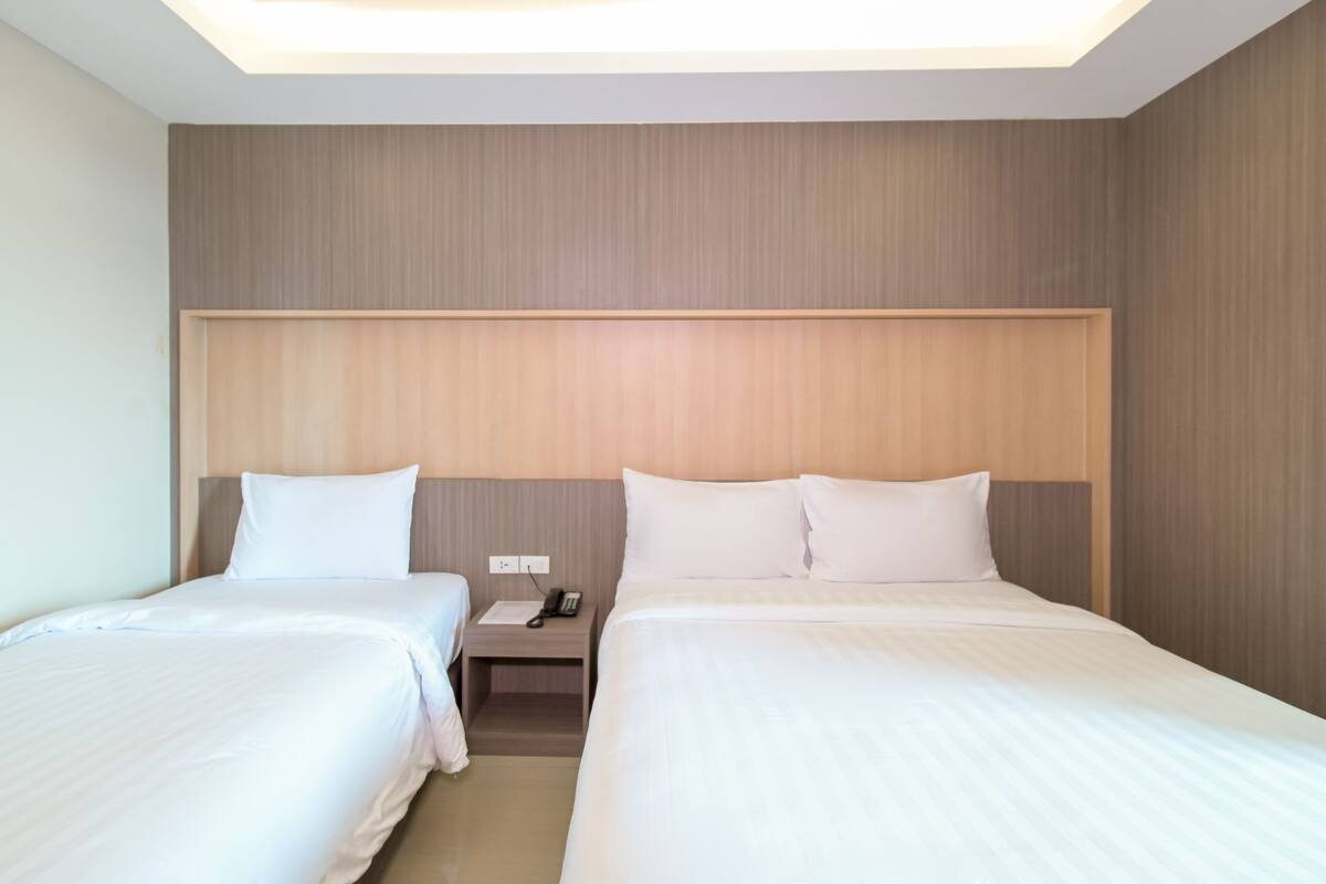 Habitación de hotel con dos camas, cabecera de madera, mesita de noche con teléfono y lámpara sobre las camas.